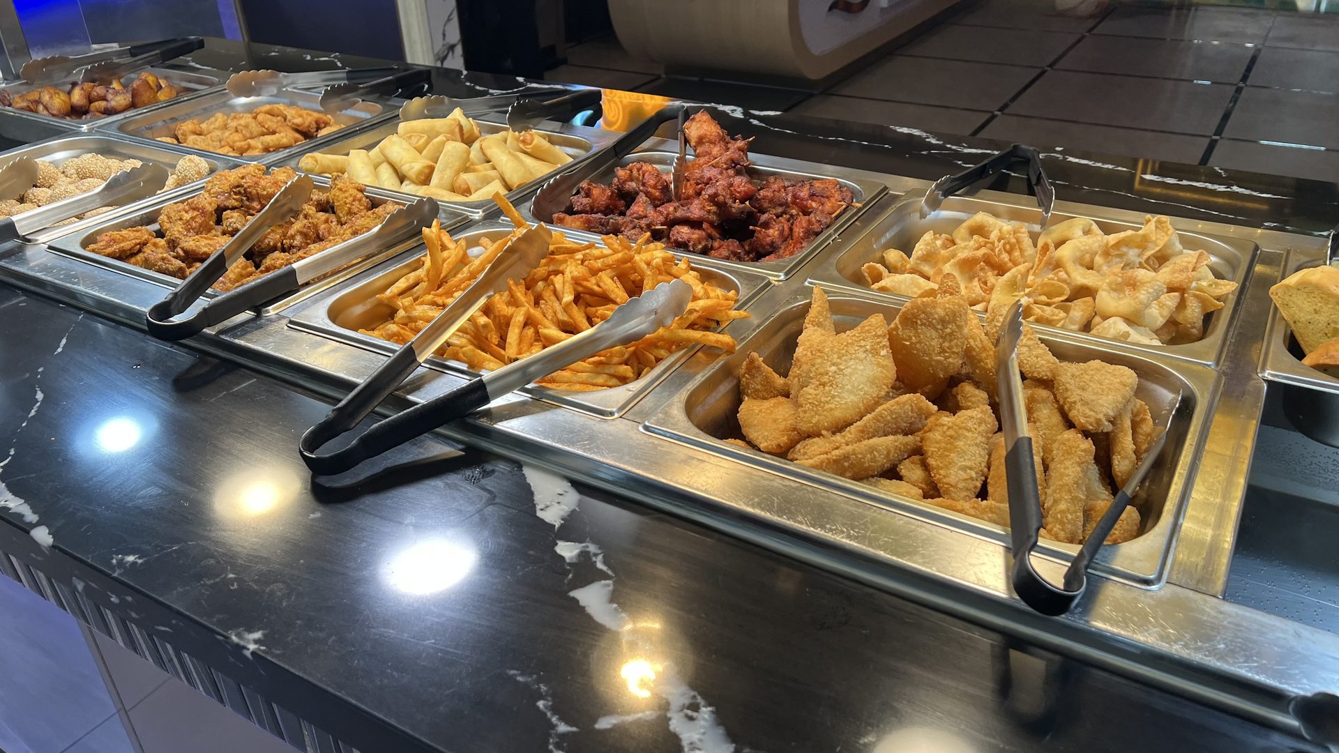 The hot buffet line: steam-table pans of spring rolls, fried chicken wings, crab rangoon, sesame balls, fries and breaded shrimp under the warming lights